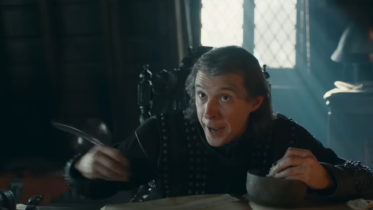 Plummer the Steward holds a quill sitting at a desk with a big book on A Knight of the Seven Kingdoms