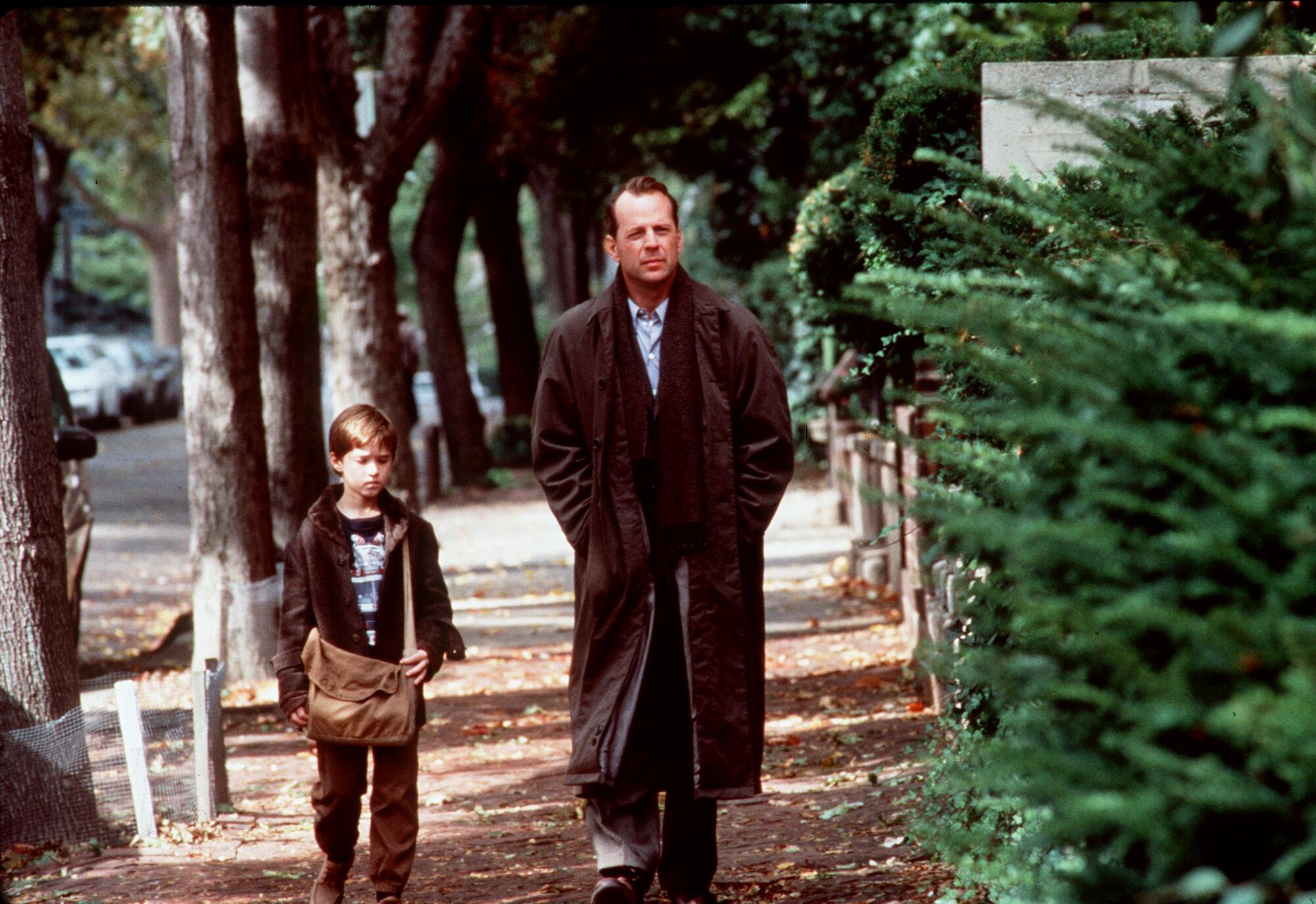 A boy and a man walk side by side on a tree-lined street.