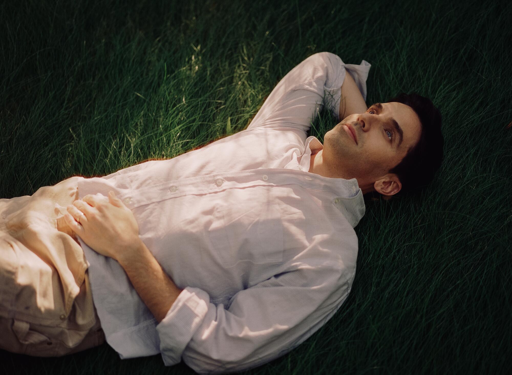 Paul W. Down lies down in the grass with sunlight dappling his face.