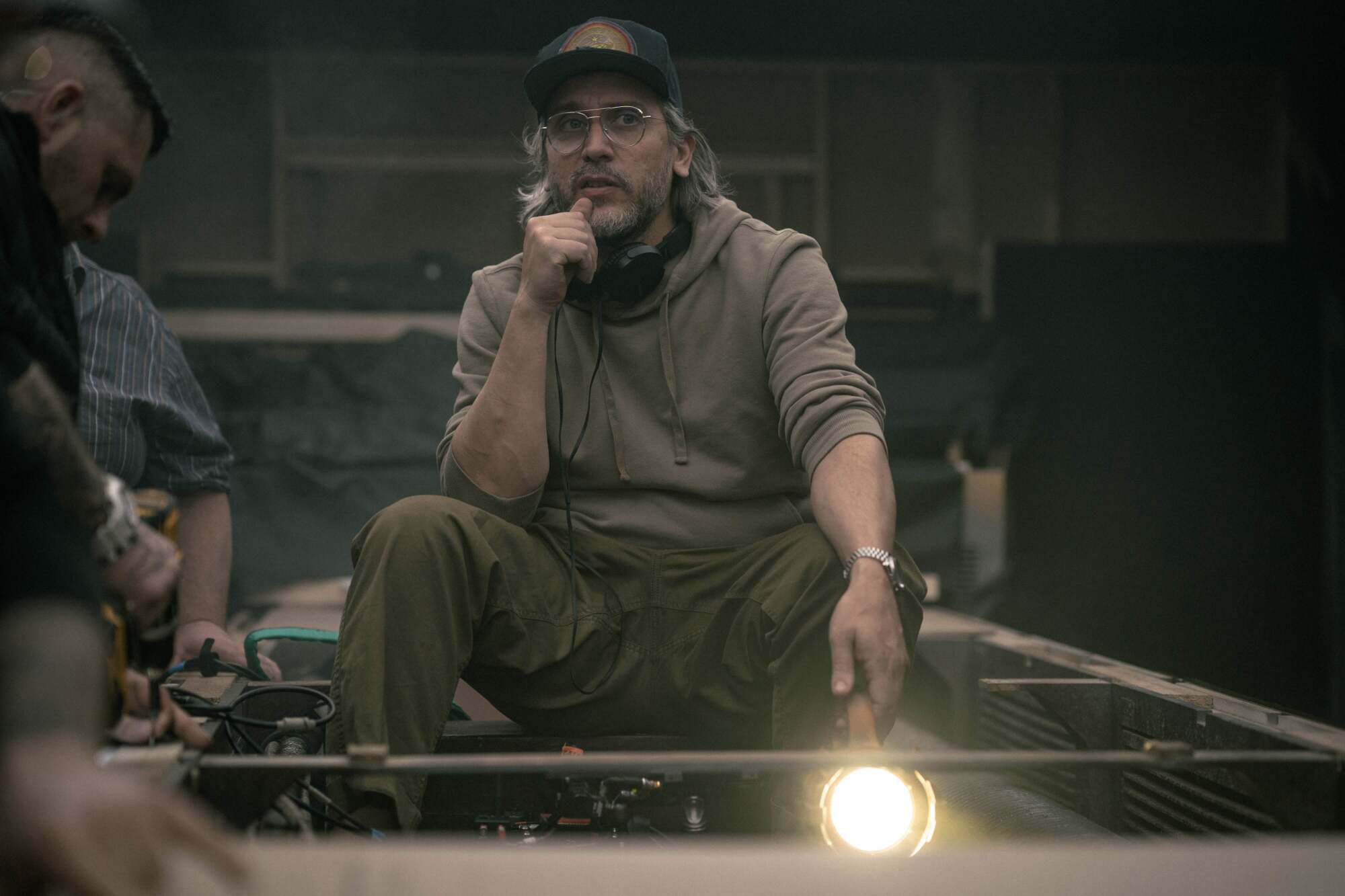 A director in a baseball cap strategizes a shot on a film set.