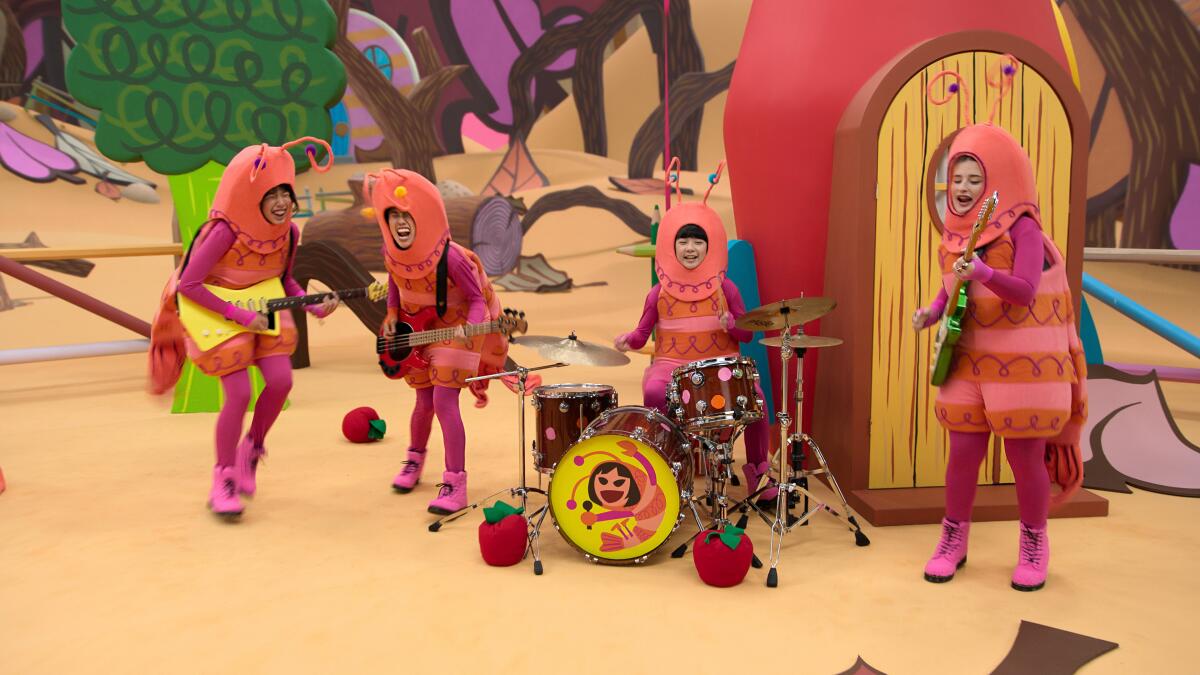 A rock band dressed as pink shrimps performs on a colorful stage.