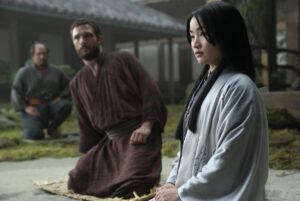 A man and a woman in kimonos kneel on mats in a garden in "Shogun."