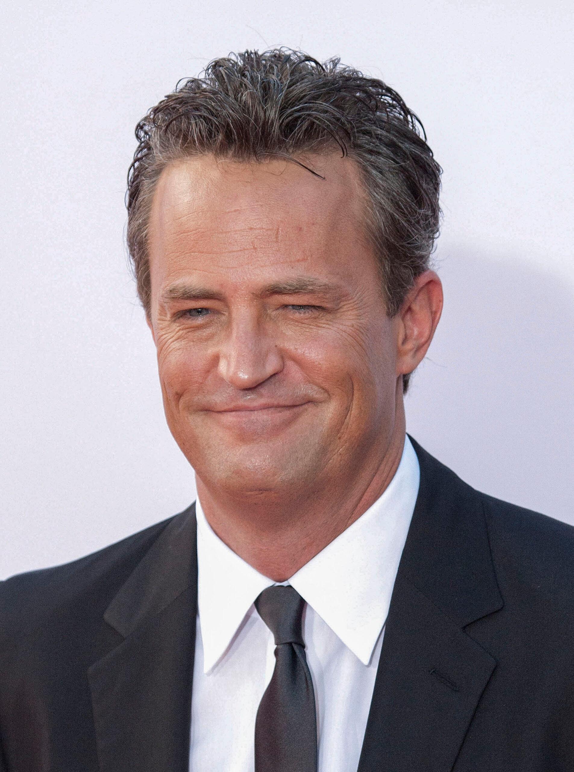 Matthew Perry smiling while wearing a suit