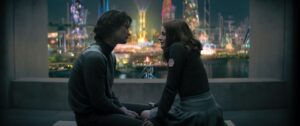 Peris (Chase Stokes) and Tally (Joey King), two young people who don’t know they’re living in a future dystopia yet, sit together and look at each other in a dark room, in front of a huge window showcasing a neon-lit city, in Netflix’s adaptation of Scott Westerberg’s Uglies