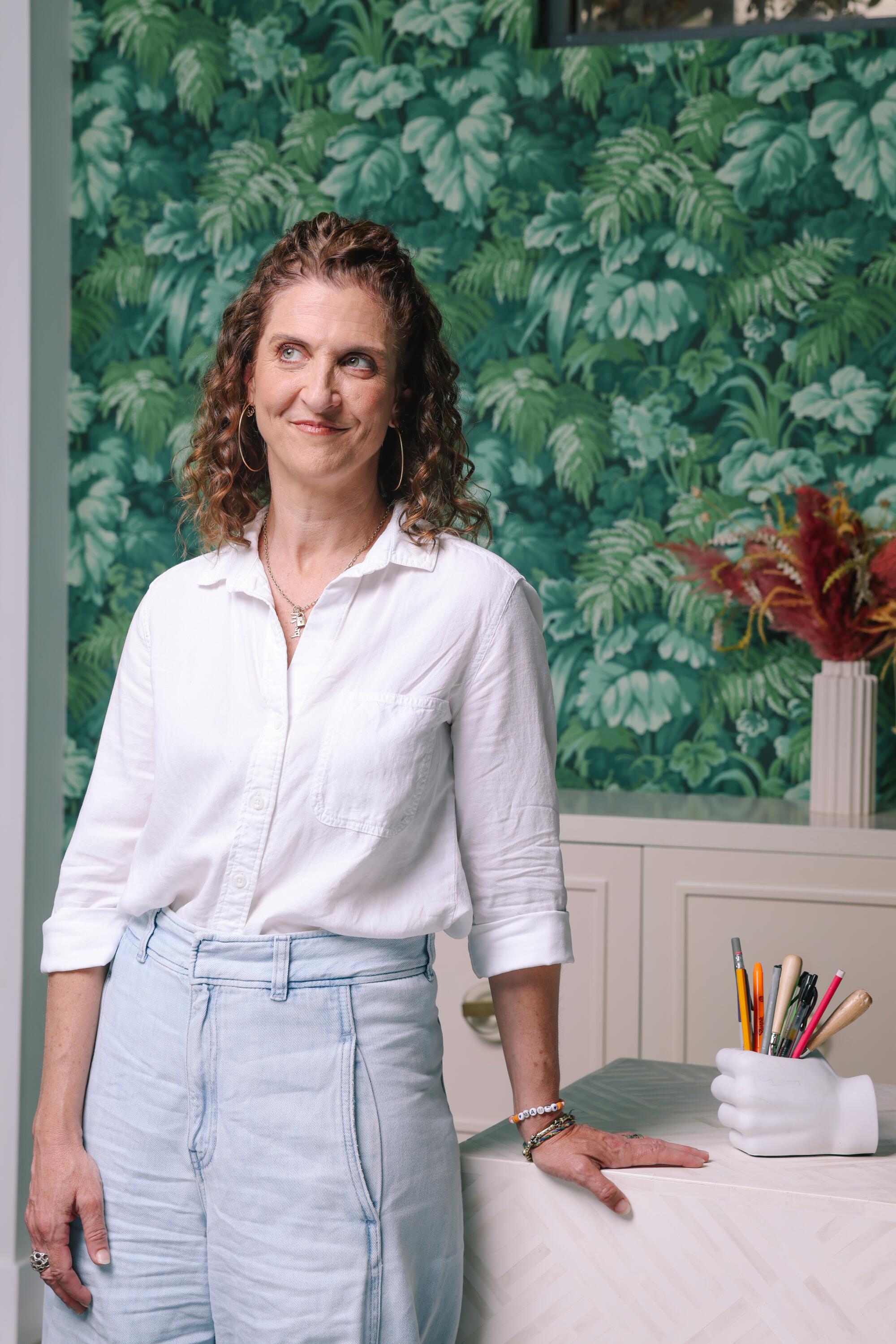 A woman with curly hair leans against a desk 