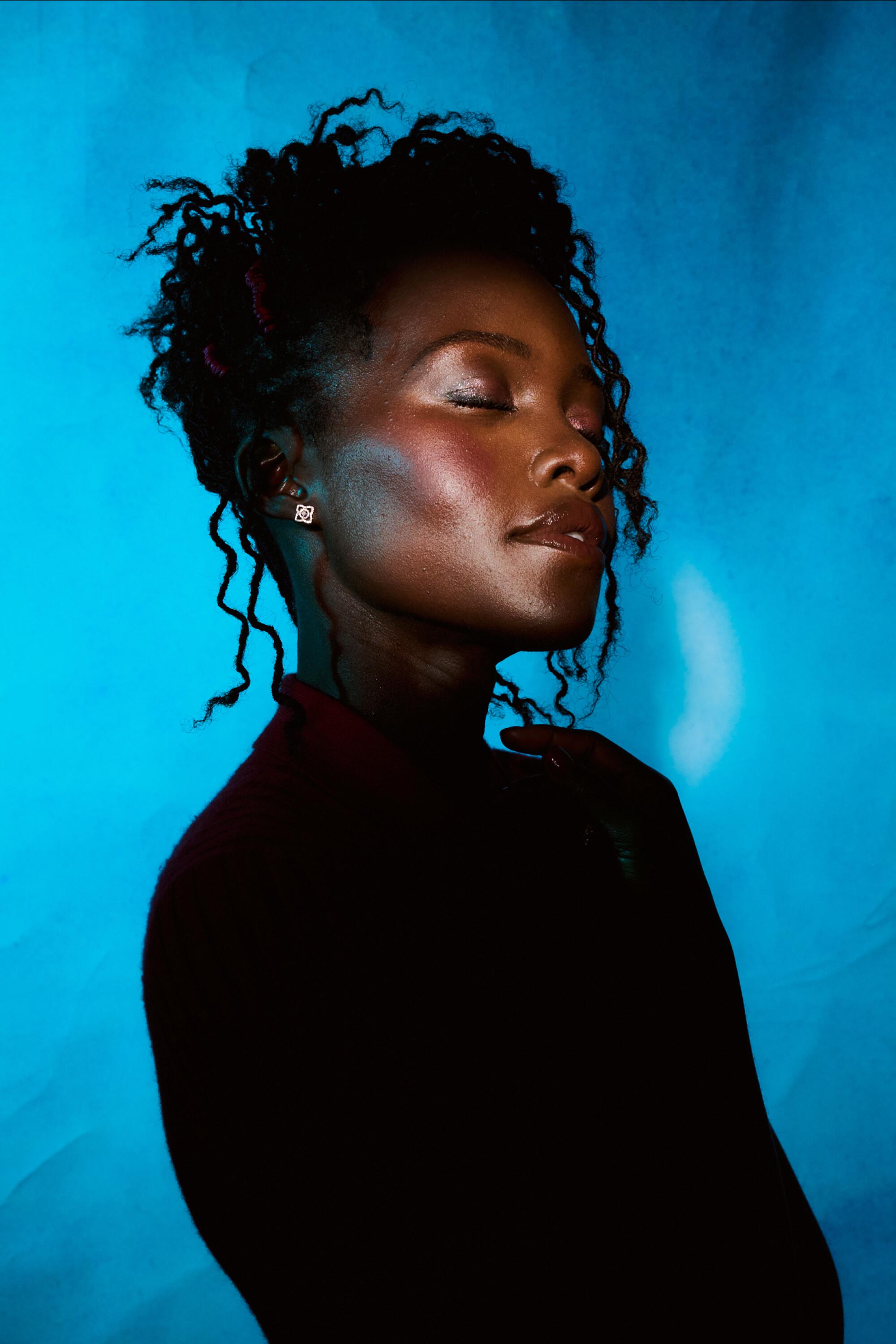 A woman with her eyes closed poses in front of a blue background.