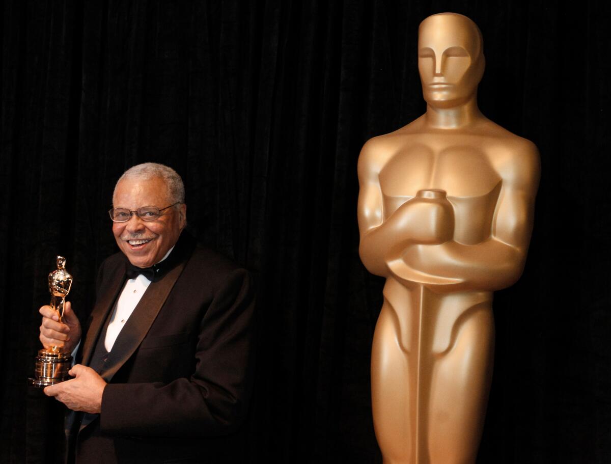 James Earl Jones holding an Oscar statuette and standing next to an oversize statue of an Academy Award 