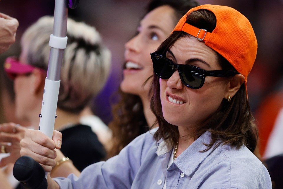 Aubrey Plaza celebrating with her crutch while sitting courtside during the 2024 WNBA All-Star Game