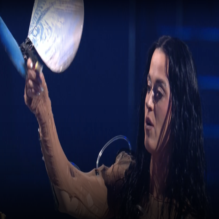 Katy Perry on stage, wearing a unique costume and holding a large seashell prop