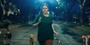 A woman runs down a street at night flanked by dogs.