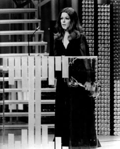 Treva Silverman stands behind a podium and holds an Emmy to her side.