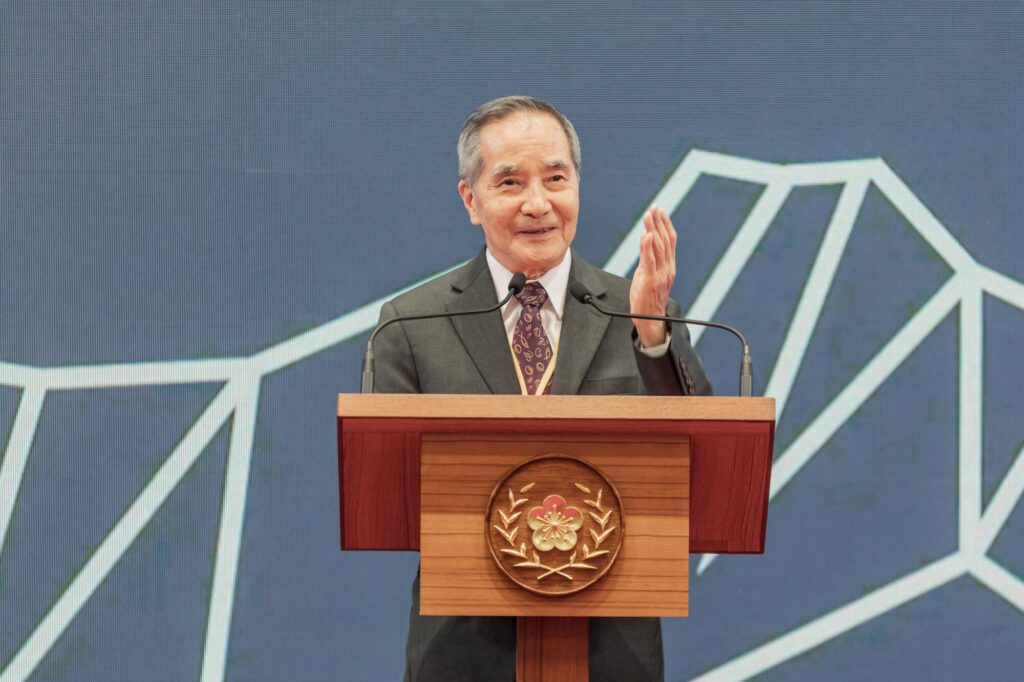 Burn Lin holds up his hand and speaks at a lectern.