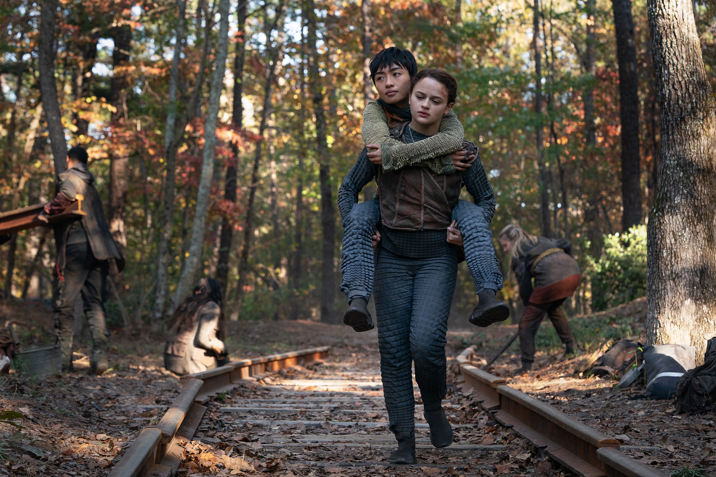 Tally (Joey King) piggy-back carries Shay (Brianne Tju) as they trek through a forest in Netflix’s Uglies.