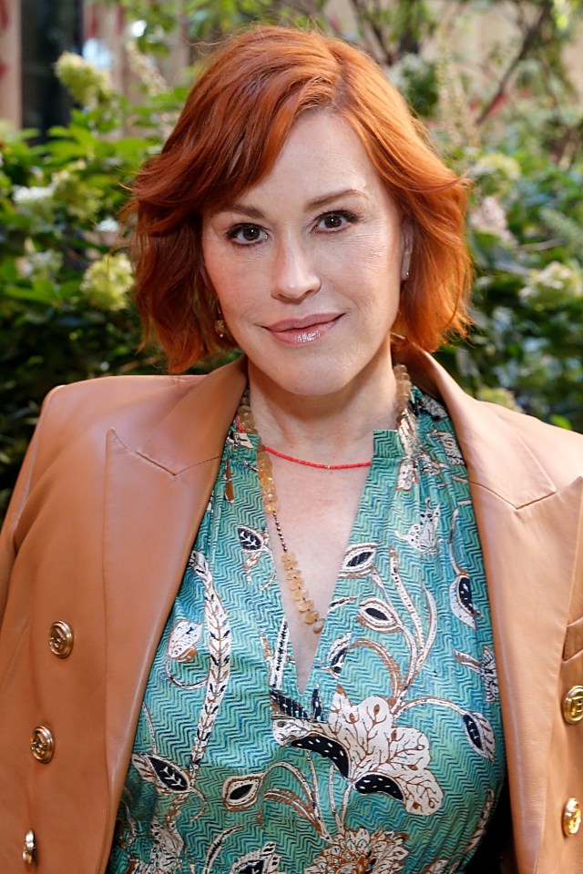 Molly Ringwald attends the Ulla Johnson fashion show in a teal green printed dress and a tan leather jacket