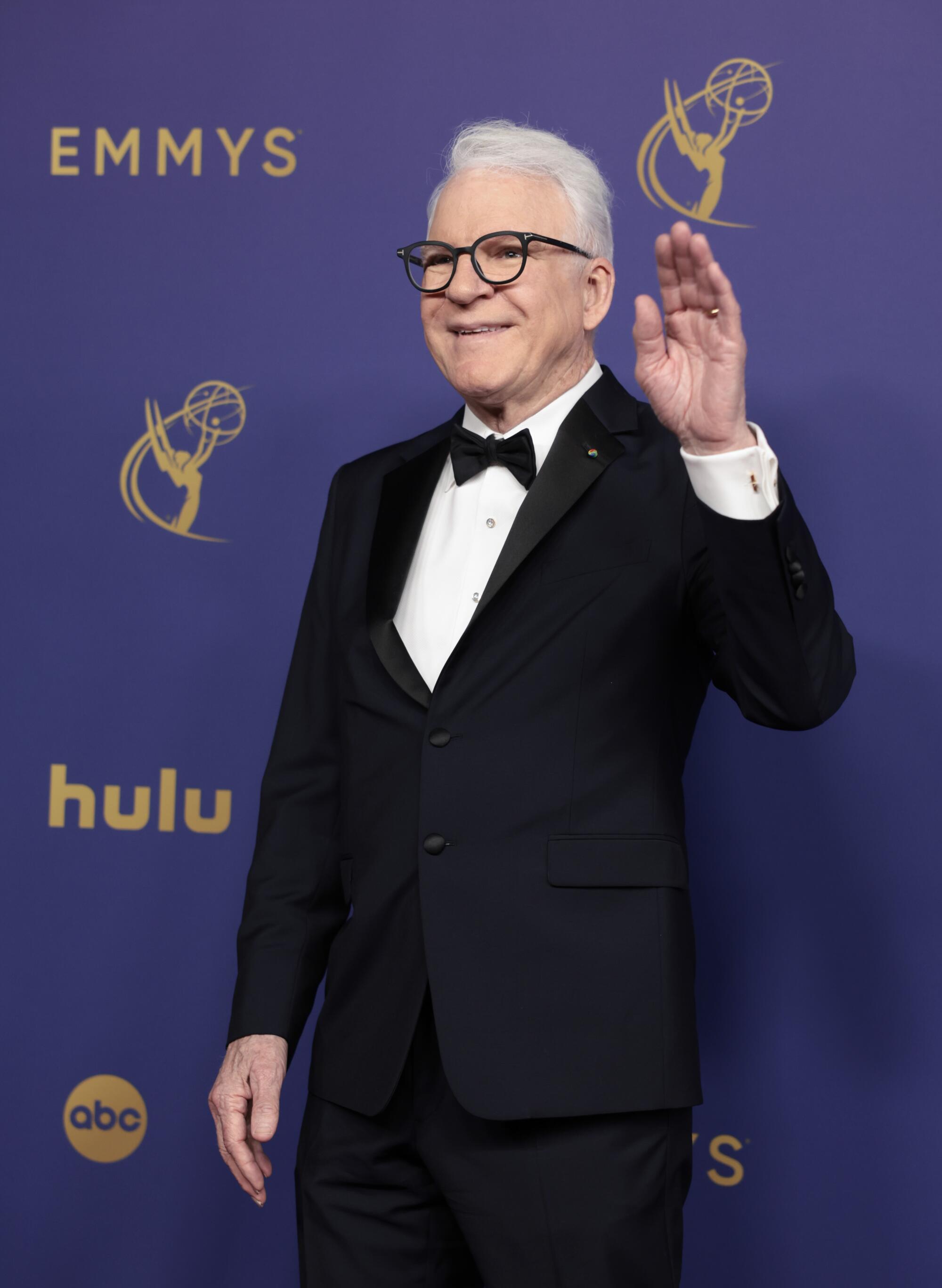 Steve Martin waves in a black suit. 