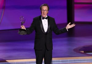 A man in a tuxedo holding a statuette with his arms extended.