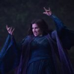 Kathryn Hahn, as Agatha Harkness, in a blue dress with her arms raised to use magic in "Agatha All Along."