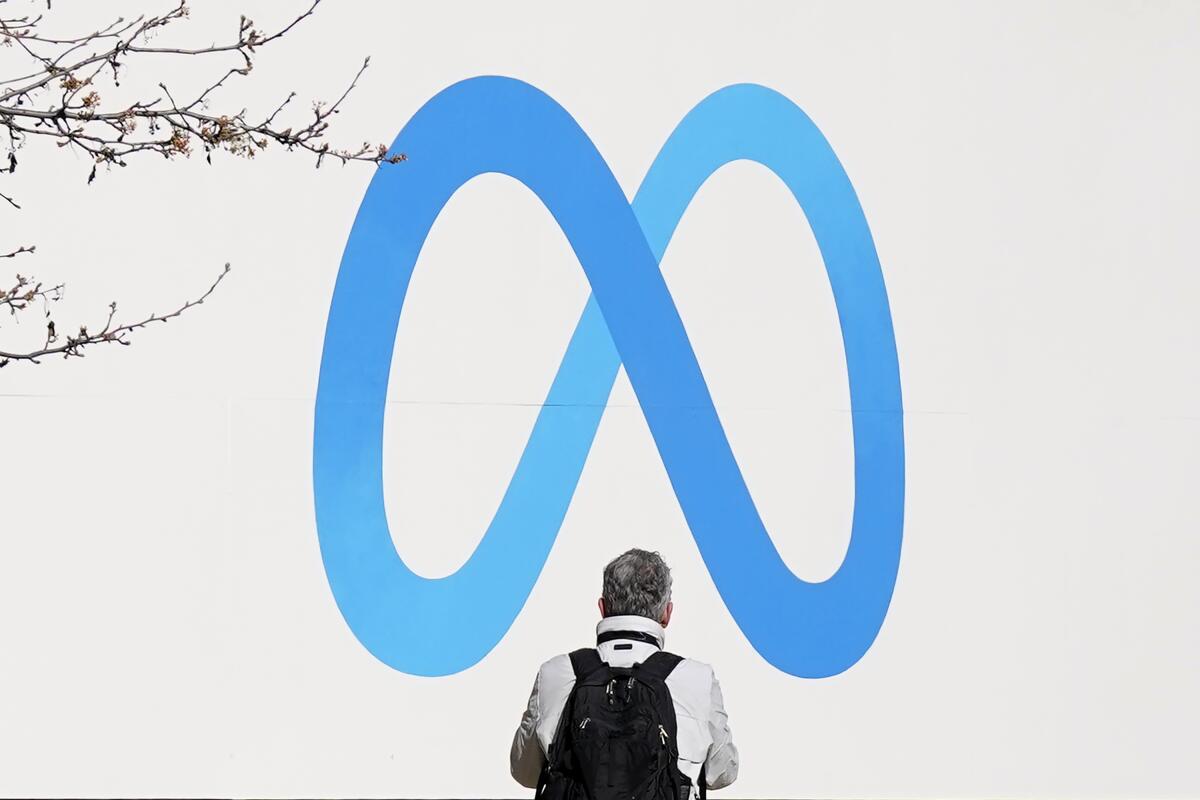 A person stands in front of a Meta sign outside of the company's headquarters in Menlo Park, Calif.