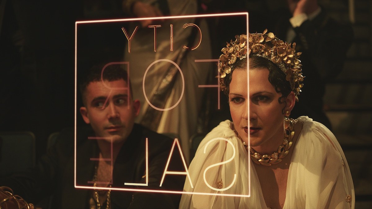 Shia LeBeouf dressed as a Roman princess and a man look at s floting translucent sign in Megalopolis