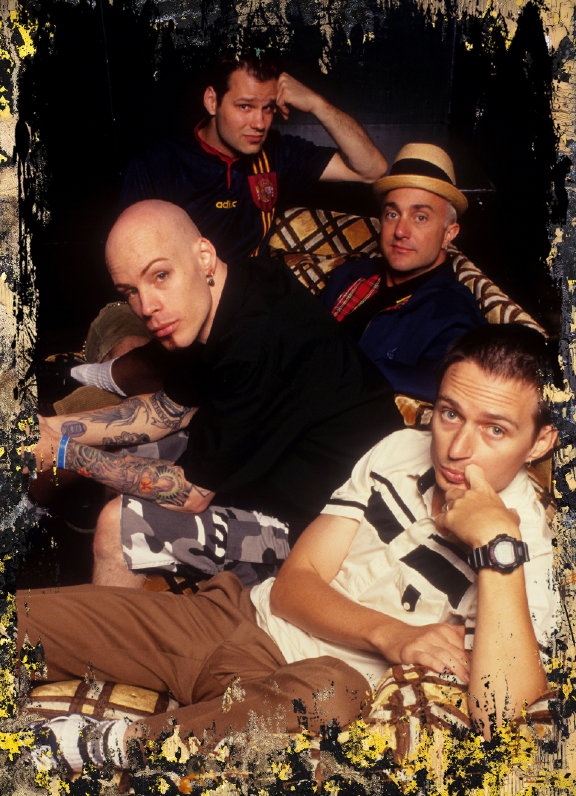 The four members of the rock band Goldfinger pose for a backstage portrait on a plaid couch.