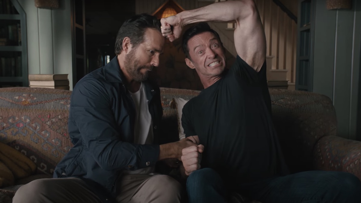 Ryan Reynolds and Hugh Jackman sitting on a couch acting out a fight between Deadpool and Wolverine