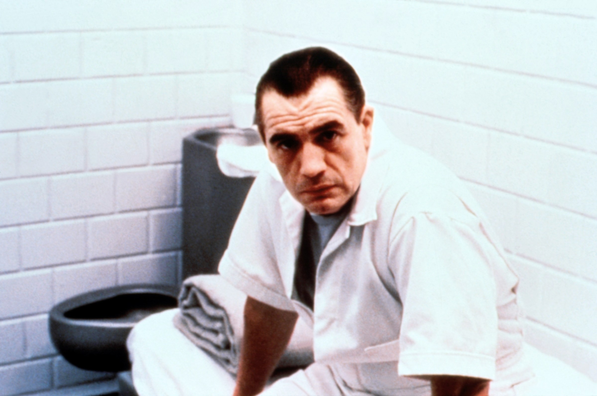 Brian Cox sits in a cell with a white prison uniform on as Hannibal Lecter in Manhunter 