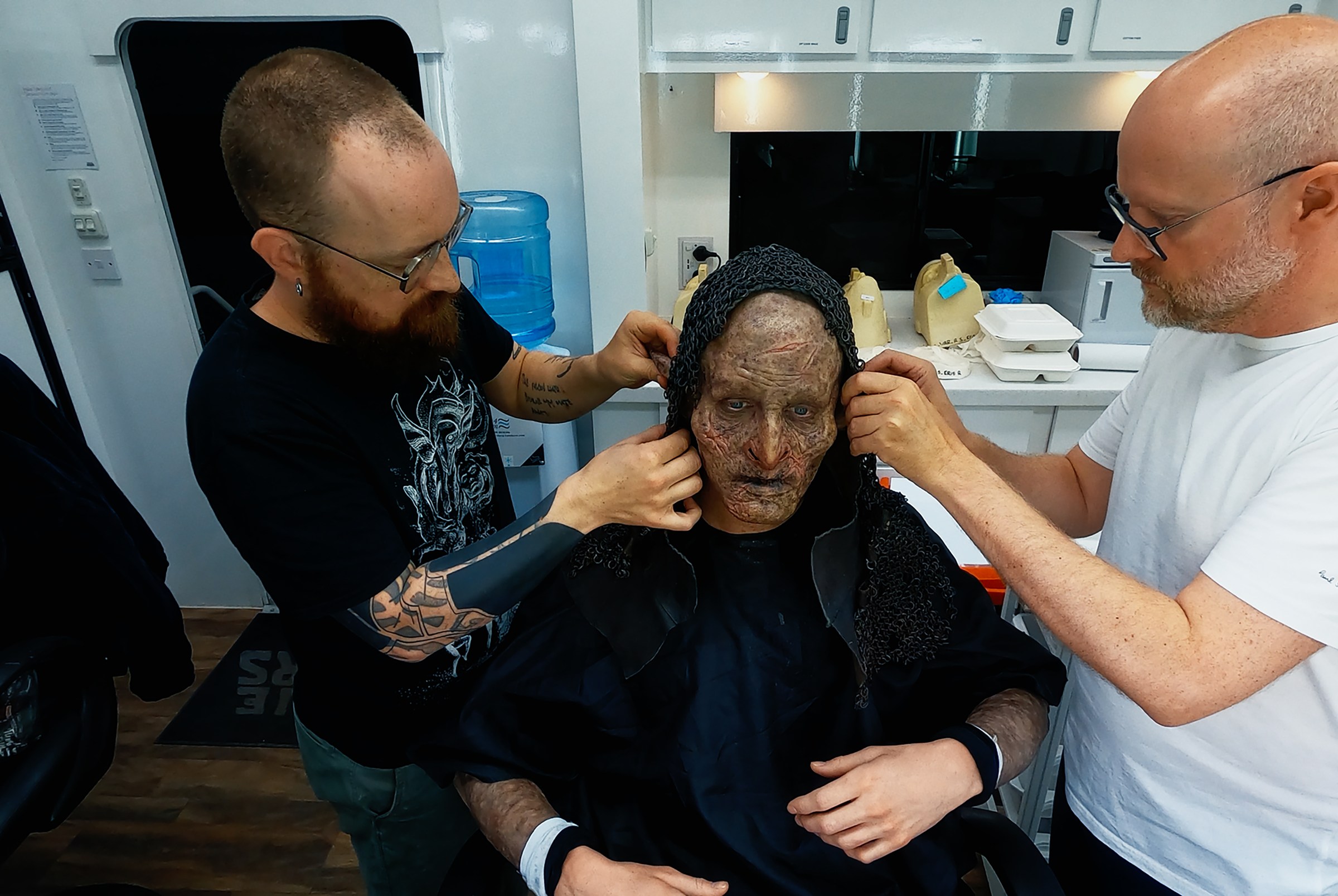 Prosthetics Artist Patt Foad (left); Robert Strange (center); and Prosthetics Designer Barrie Gower putting the balaklava over Robert Strange’s head (with orc makeup on)