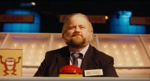 Paul Walter Hauser sits at a game show buzzer in a still from The Luckiest Man in America movie