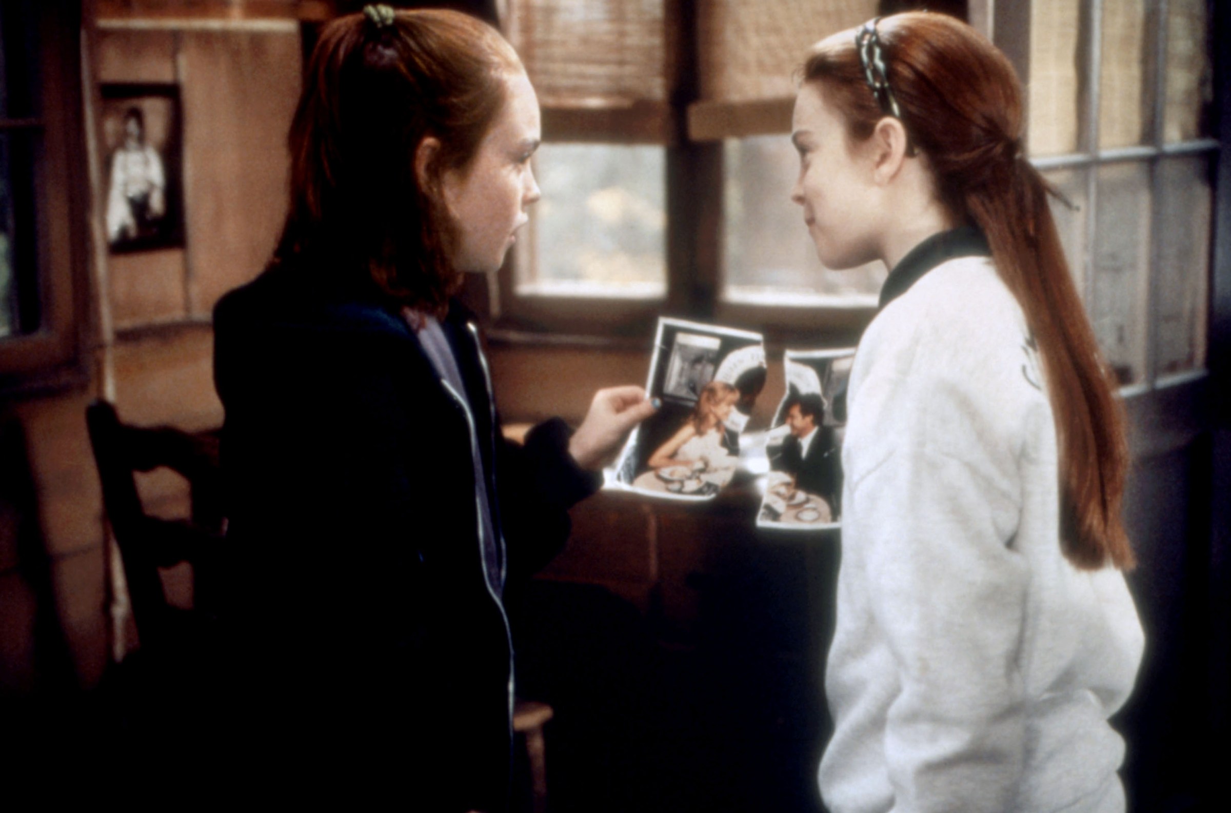 Two young Lindsay Lohans hold up torn halves of a picture together in The Parent Trap