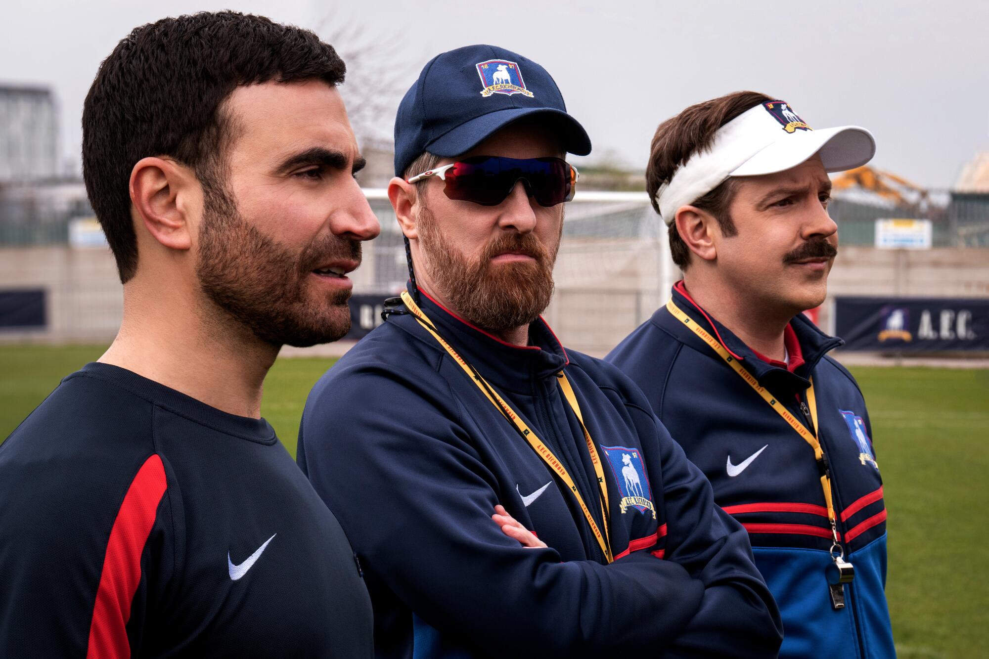 Three soccer coaches look out onto the pitch