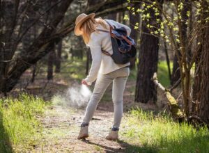 Woman wearing long sleeves and long pants sprays tick repellant on her legs