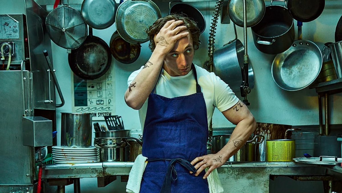 Jeremy Allen White as Carmy in the kitchen with his head on his hand wearing a blue apron over a white tshirt on The Bear, The Bear was a big winner at the 2024 Emmys