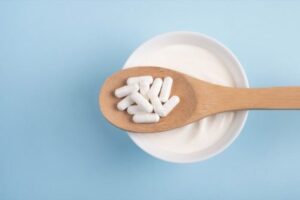 probiotic capsules on wooden spoon over yogurt bowl