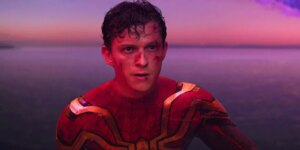 Tom Holland looking angry as Spider-Man. against a blue and purple background, with cuts on his face and sweaty hair