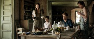 George MacKay, Mia Goth, and Charlie Heaton sit around a table in Marrowbone