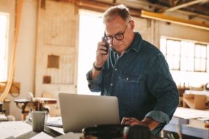 Senior man talking on cell phone and using laptop on work table