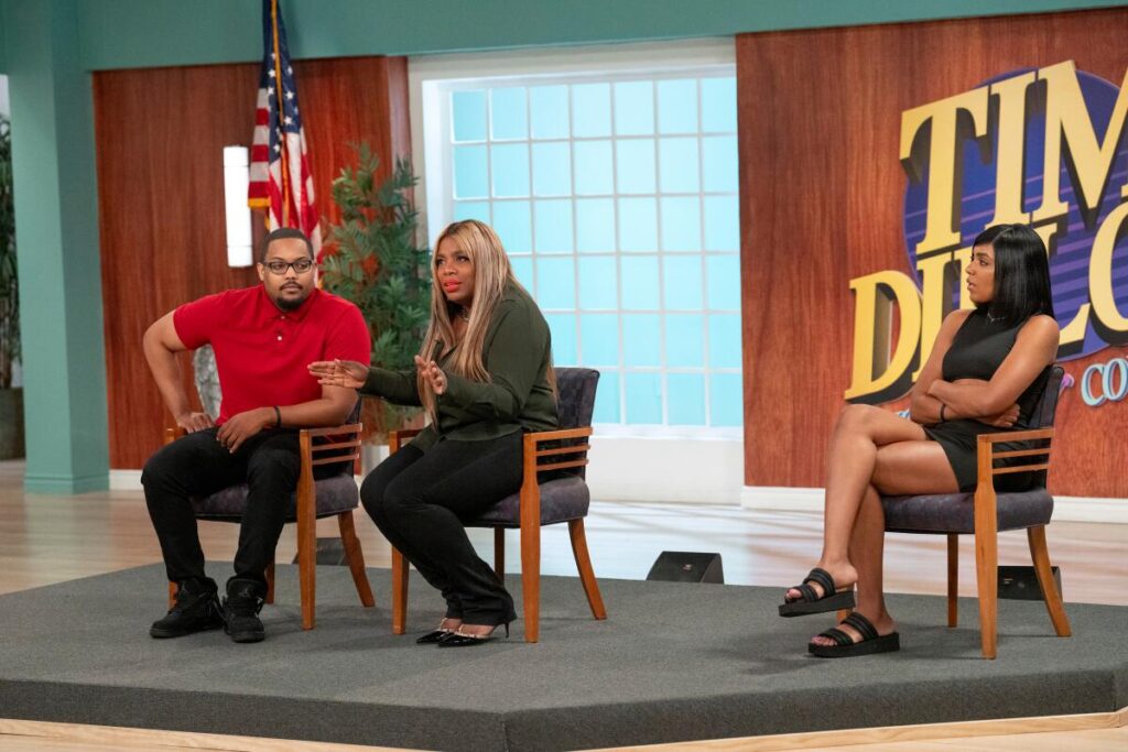 A couple sitting in chairs on a stage as a woman sitting to their left looks in their direction.