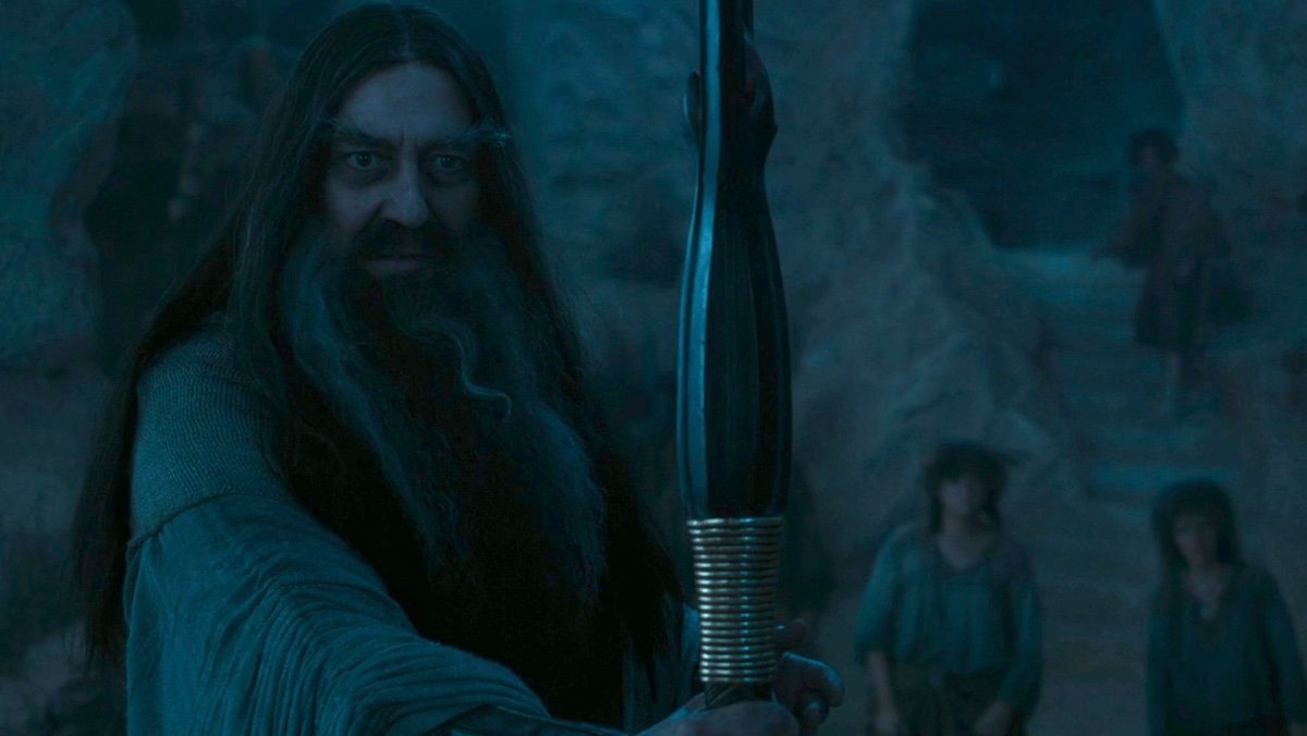 Ciarán Hinds as the bearded Dark Wizard holding his staff out in the dark on The Rings of Power