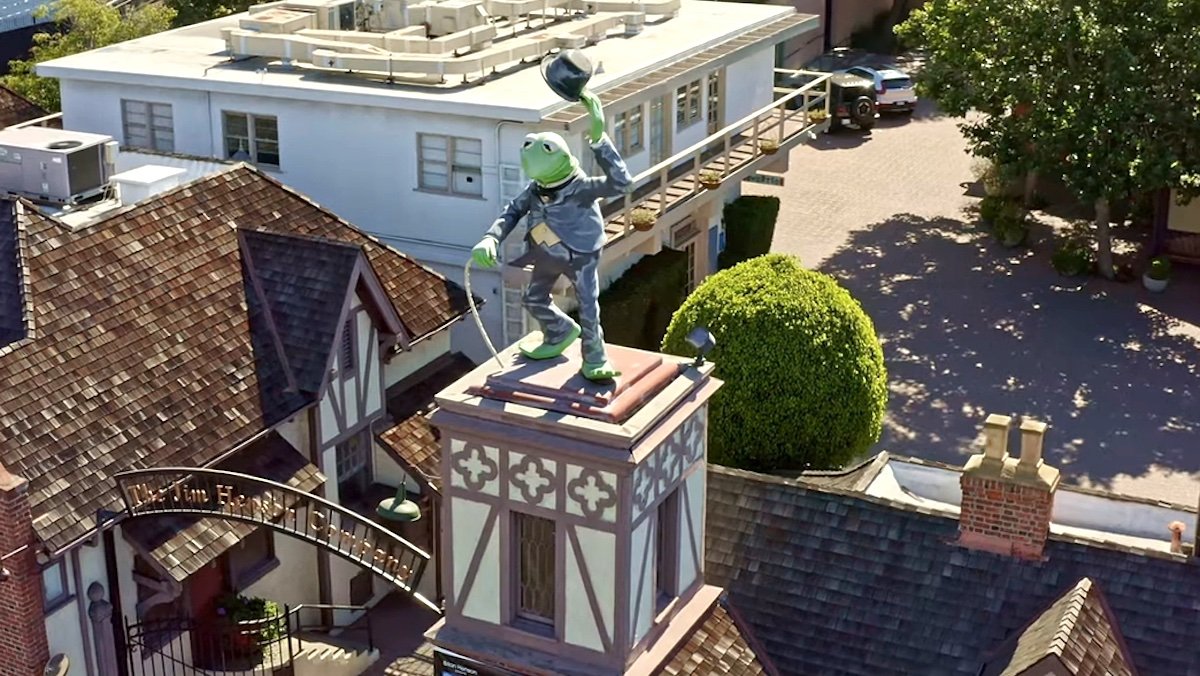 A Kermit the Frog dressed as Charlie Chaplin's the Tramp statue atop the gate of the Jim Henson Company Lot as seen from a drone