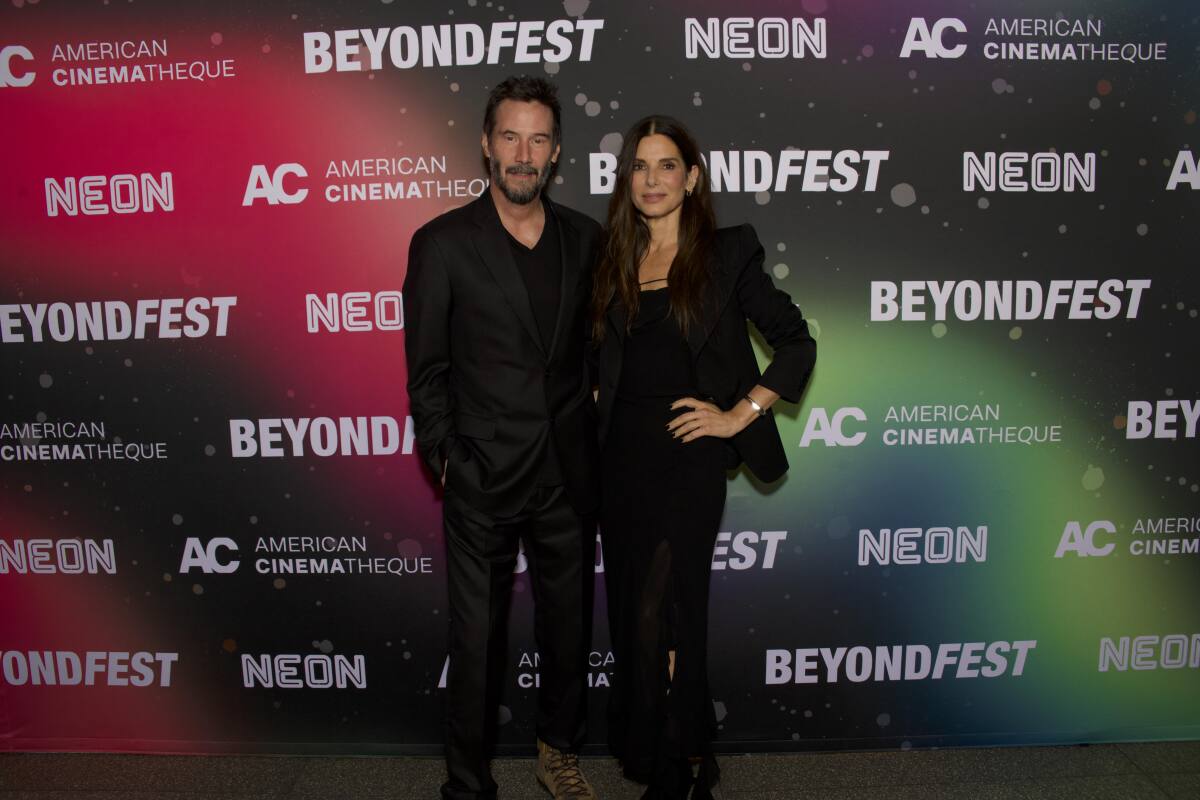 Two people  in dark clothes pose at a screening event.