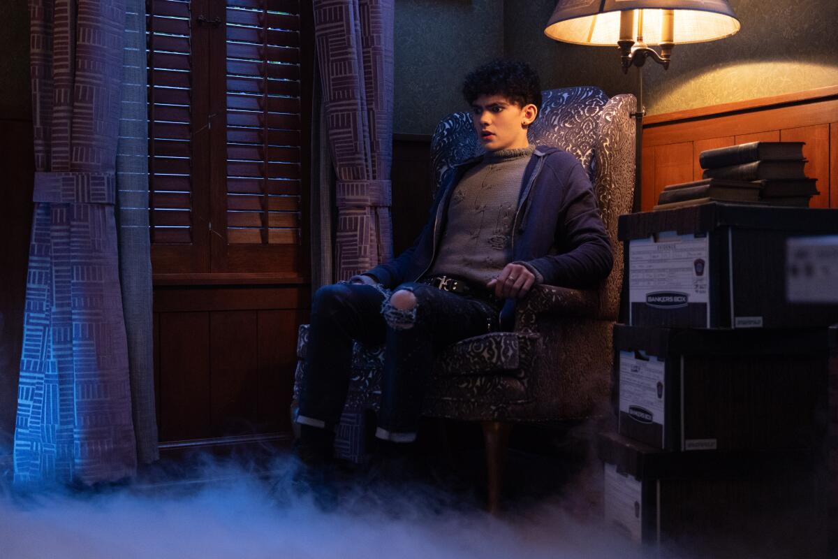 a teenage boy in a dark hoodie and jeans sitting in a chair