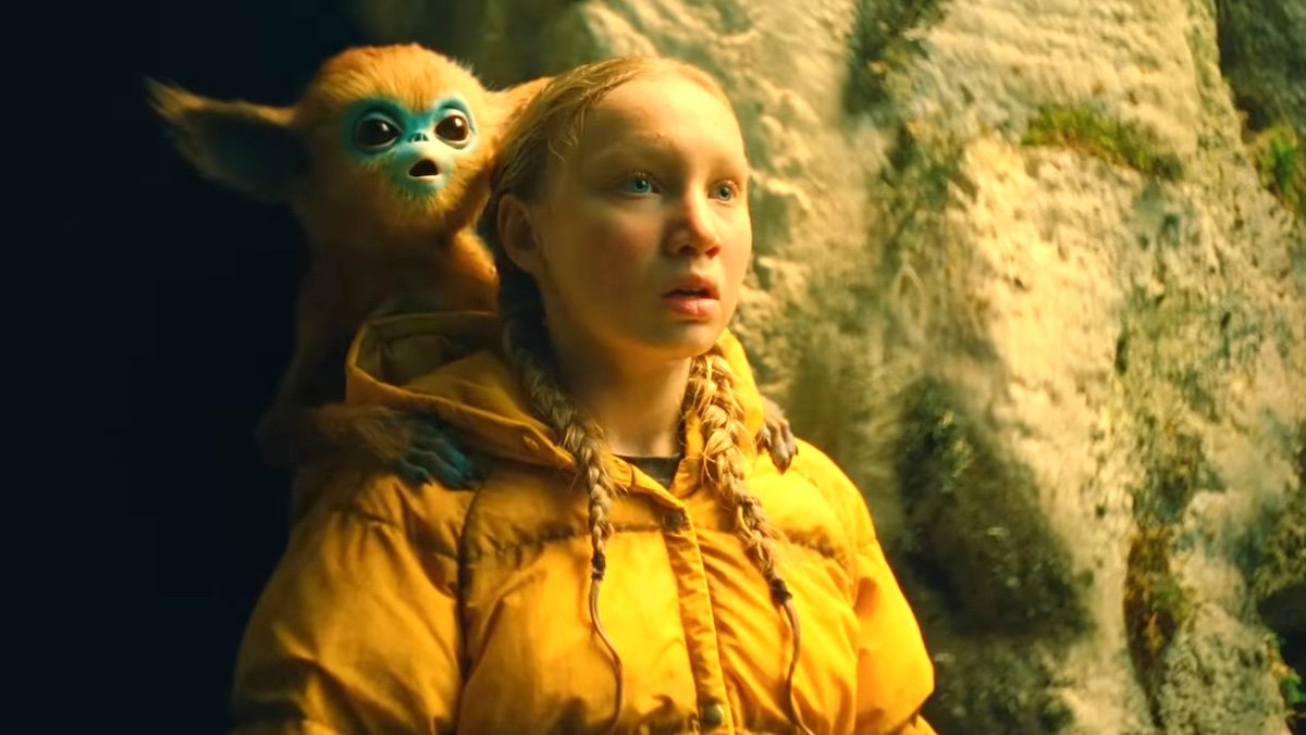 A young girl in a yellow coat with a strange furry creature on her shoulder in The Legend of Ochi