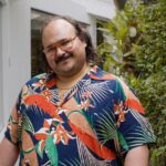 A man in a boldly patterned shirt smiles for the camera.