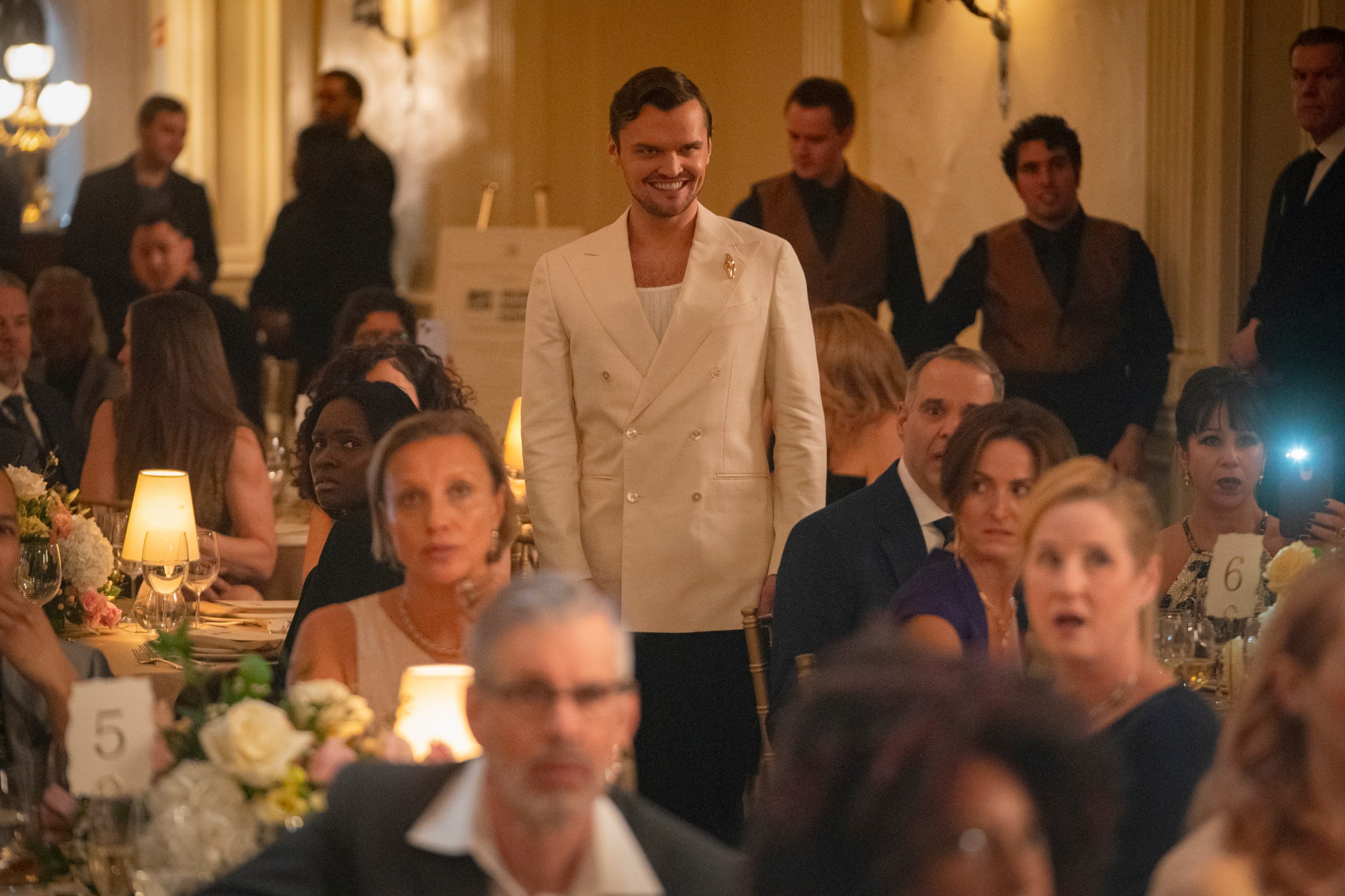 Ray Nicholson stands up at a black tie event wearing a white jacket and a sinister grin on his face in Smile 2 