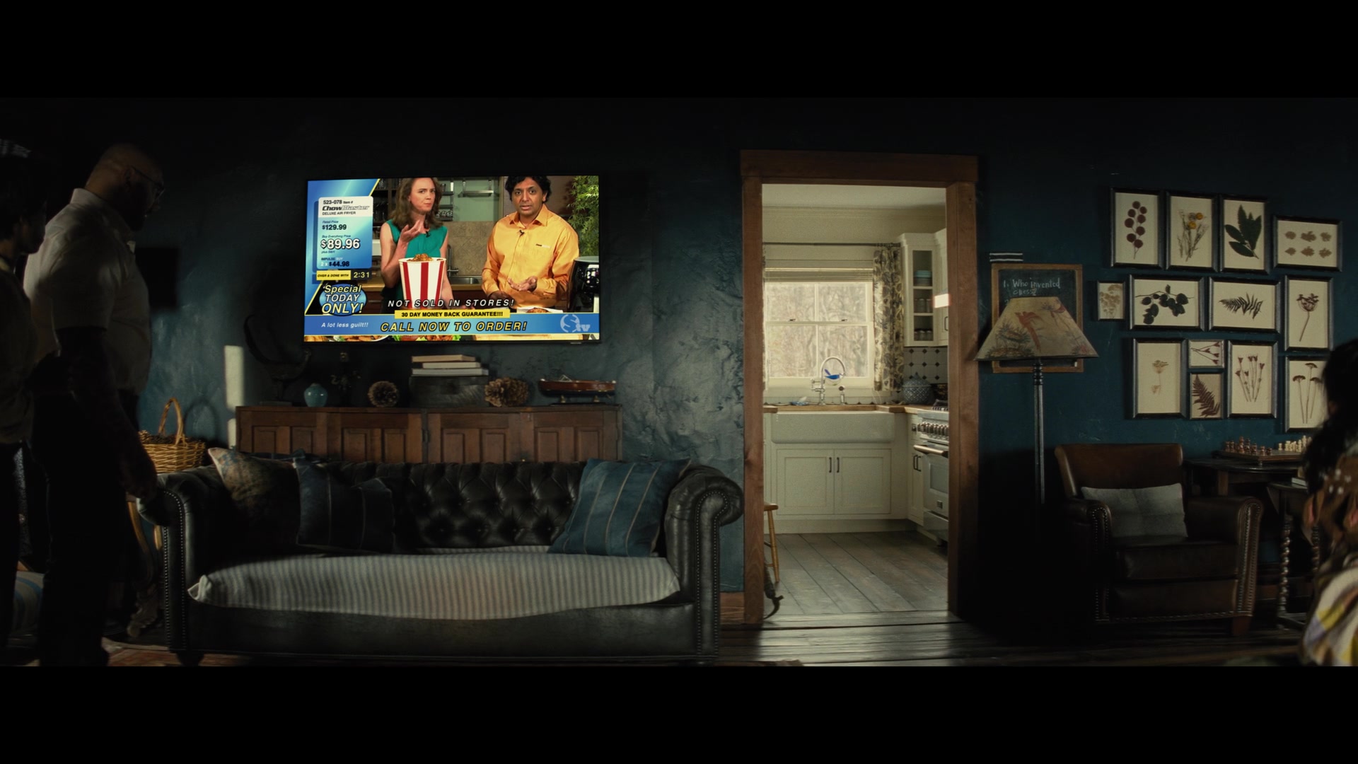 An image from Knock at the Cabin with Dave Bautista at the edge of the frame while M. Night Shyamalan is on the TV 