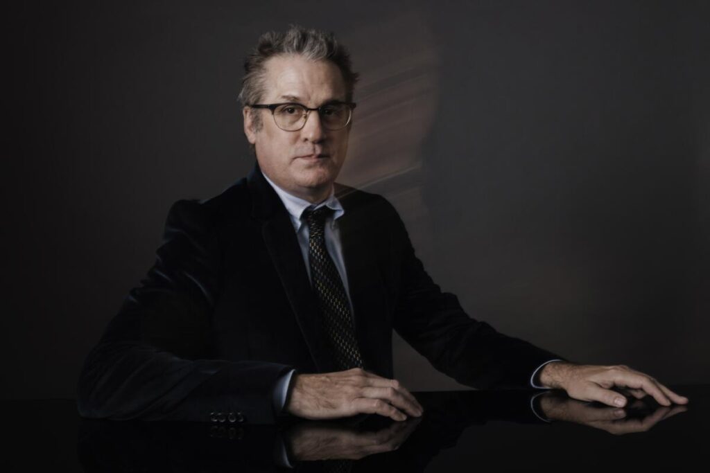 A man in glasses and a dark suit and tie.