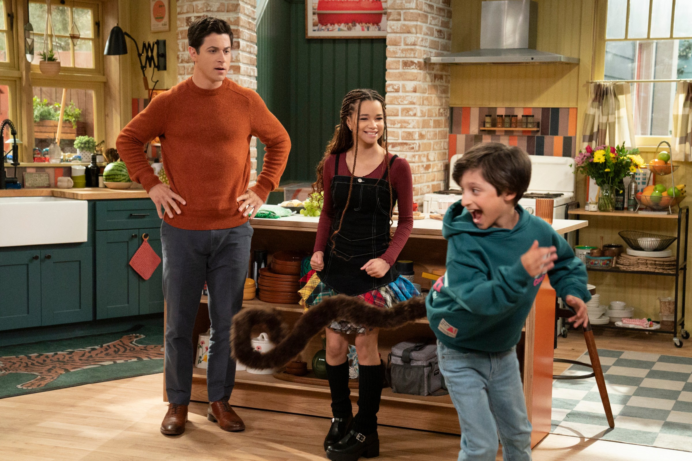 Justin looking disapproving as his son shakes a long, brown, furry tail added to his body with magic. Billie looks happy. From Wizards Beyond Waverly Place.