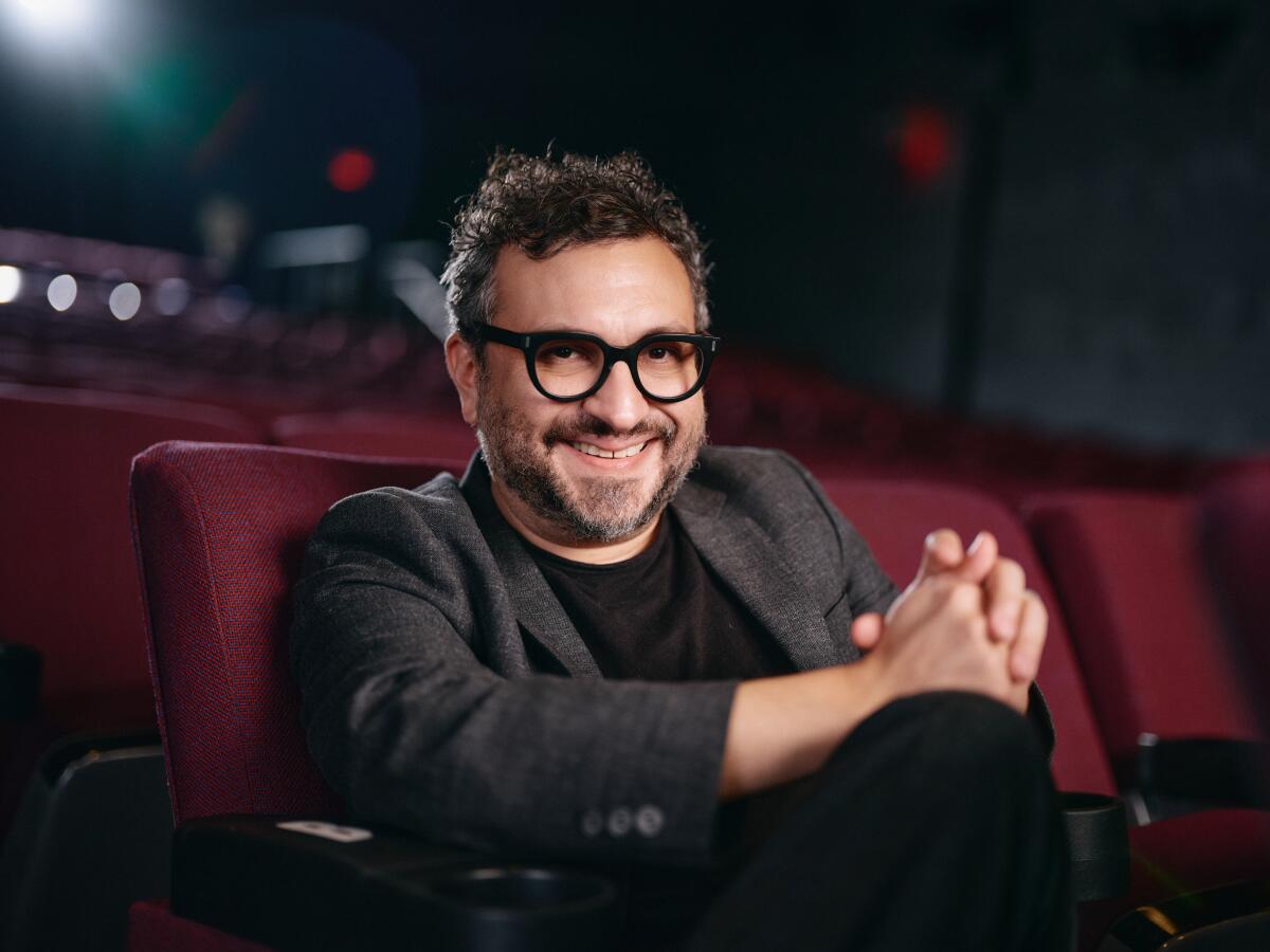 A man in a blazer smiles in an empty movie theater.