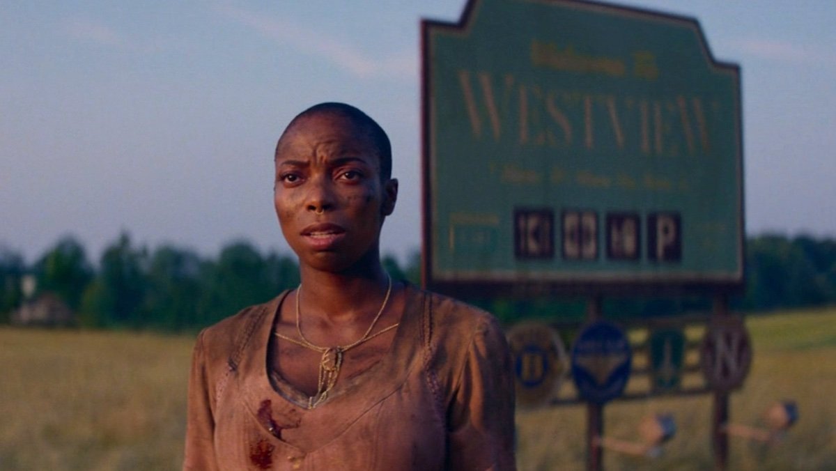 A muddied Jen kale standing before the Westview town sign on Agatha All Along