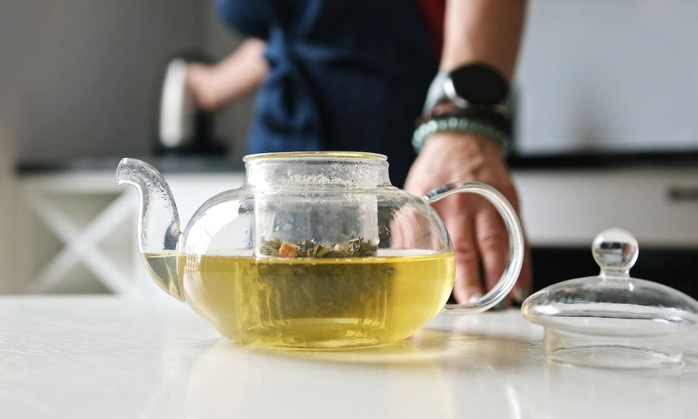 closeup of a person brewing a small pot of green tea in a glass kettle